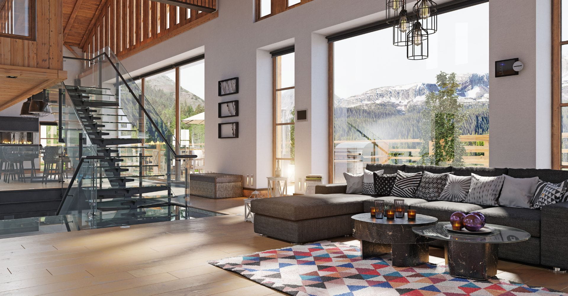 Modern living room with large windows, mountain views, and natural light. Features a glass staircase, gray sectional sofa, geometric rug, and hanging lights. Cozy and spacious atmosphere.