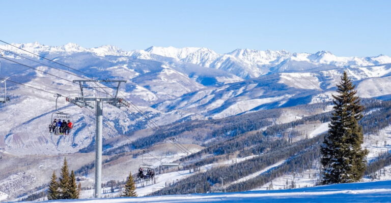 A ski lift ascends snowy mountains, surrounded by a stunning winter landscape under a clear blue sky.